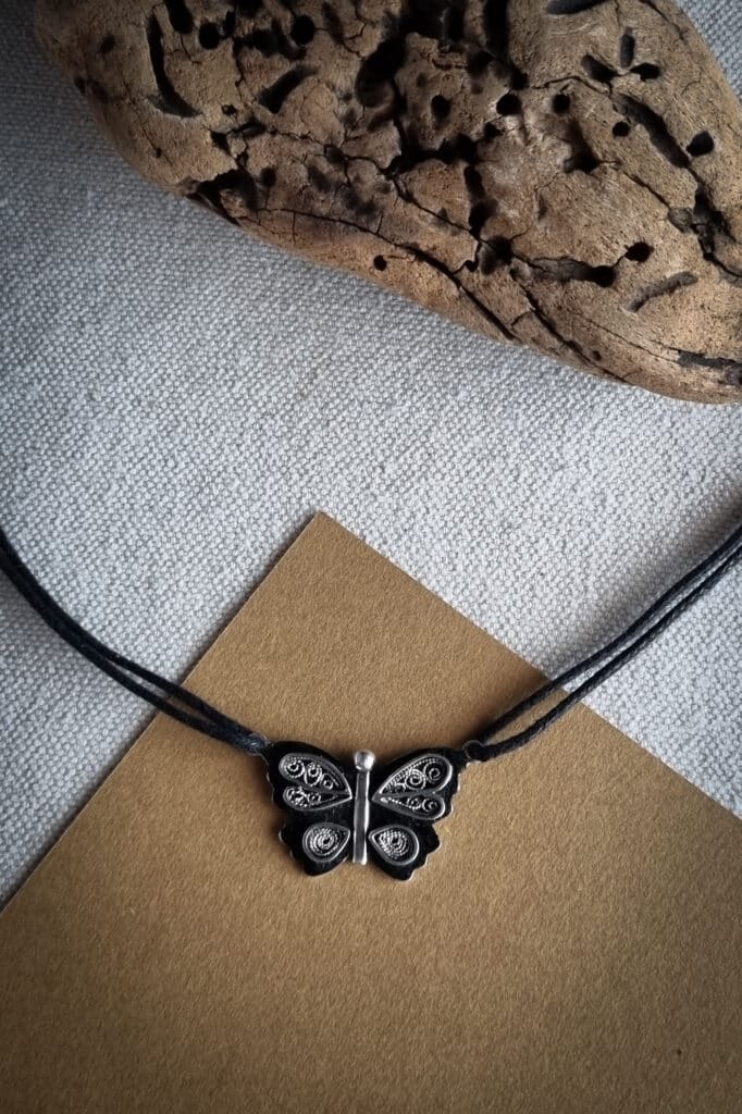 collier avec pendentif en argent papillon en filigrane sur un fond noirci