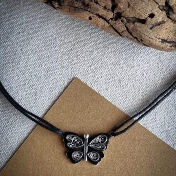 collier avec pendentif en argent papillon en filigrane sur un fond noirci