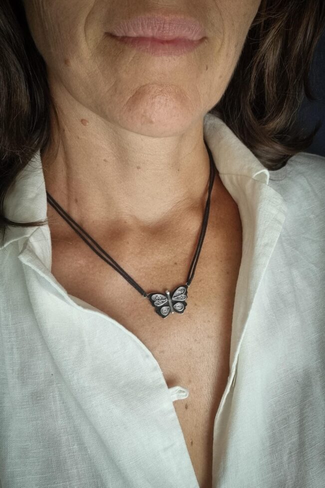 collier avec pendentif en argent papillon en filigrane sur un fond noirci