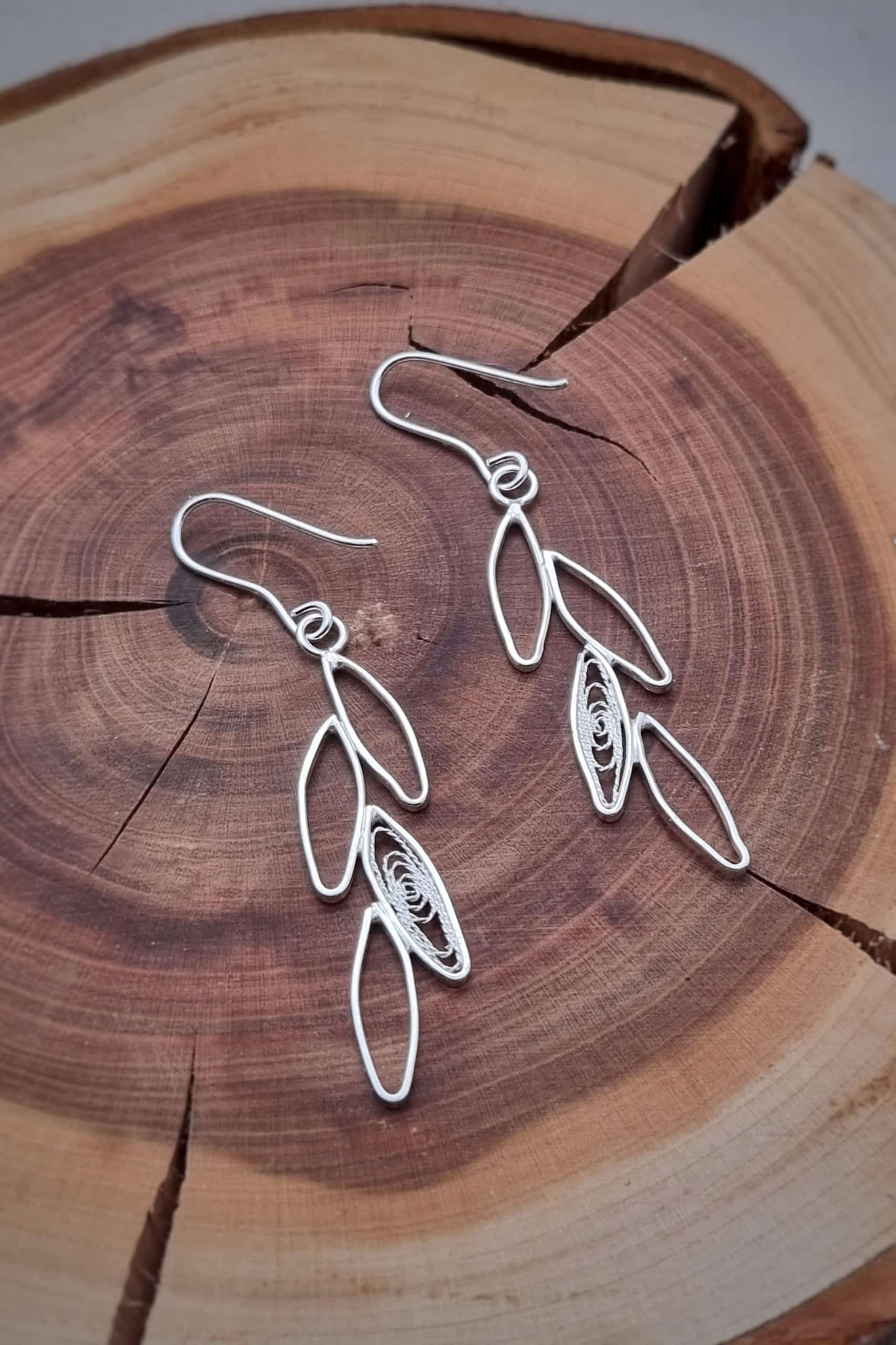 Boucles oreilles feuille filigrane sur l'envers posées sur un rond de bois