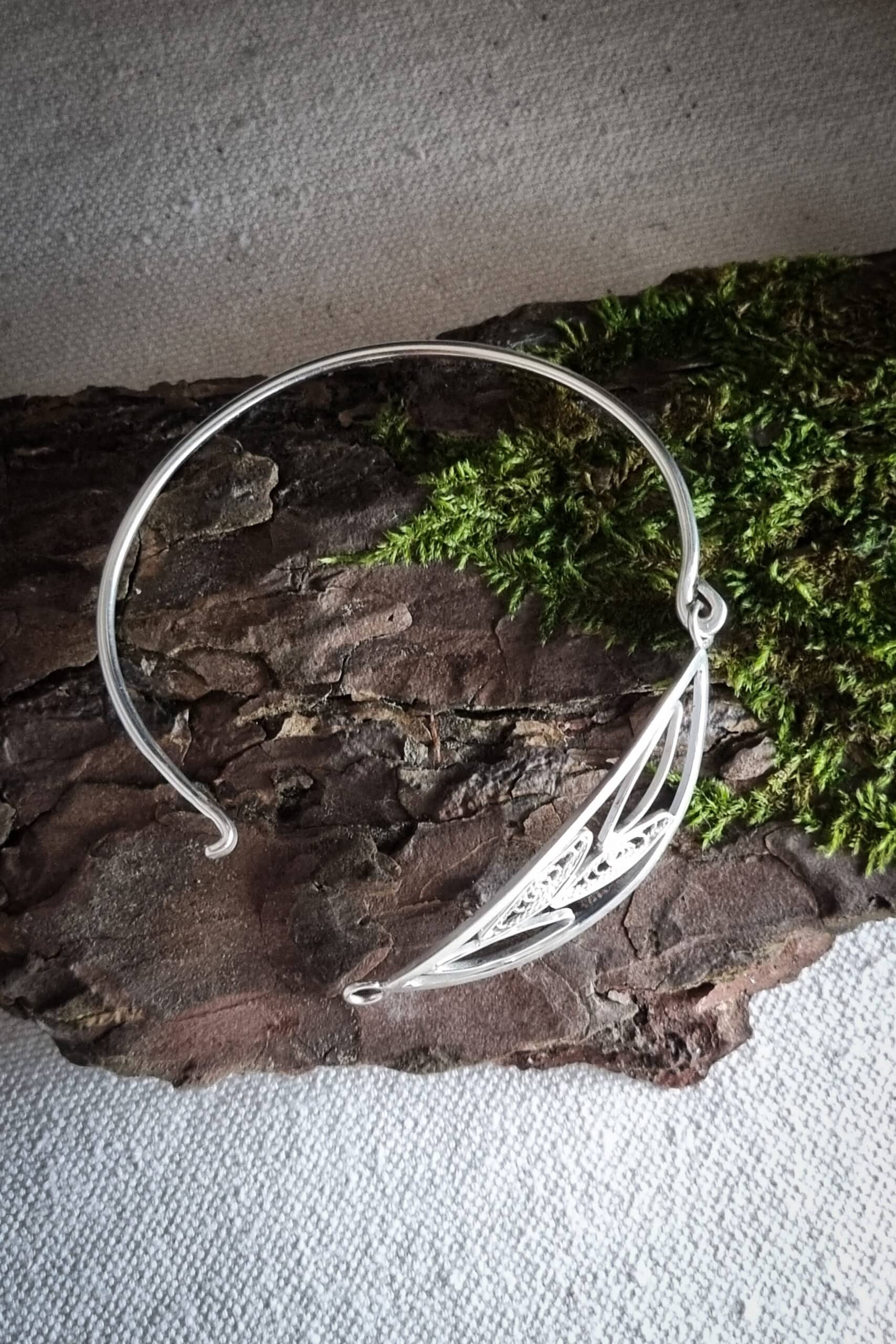 bracelet en argent avec filigrane, représentant un brin d’olivier, posé sur une écorce