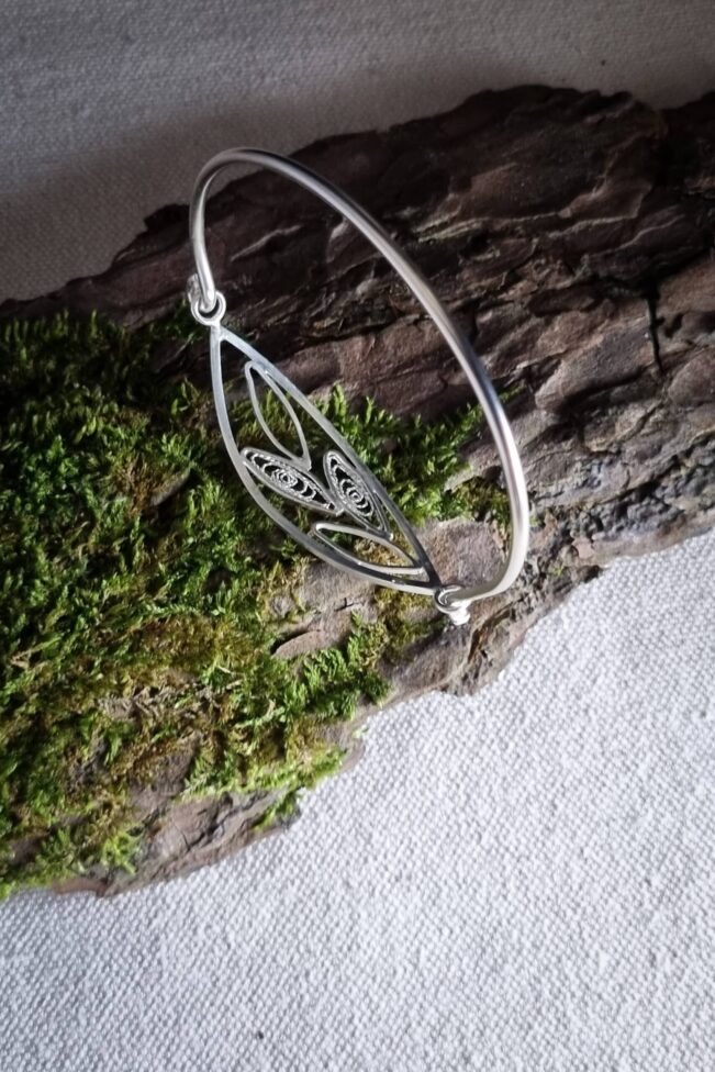 bracelet en argent avec filigrane, représentant un brin d’olivier, posé sur une écorce